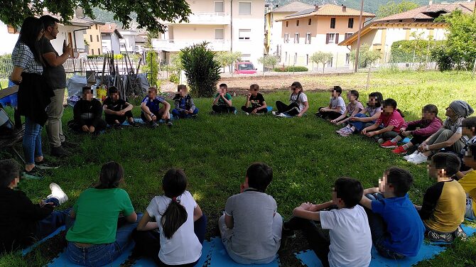 Foto di studenti seduti in cerchio in un prato mentre ascoltano la lezione dell'esperto