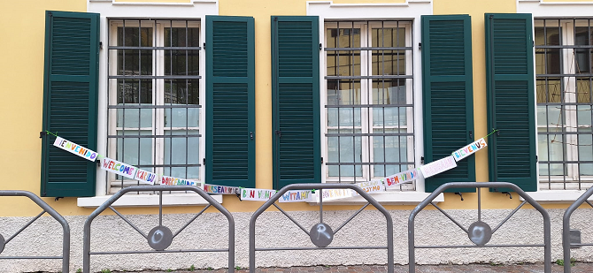 Foto delle finestra della Scuola con lo striscione fatto di parole "amici" e "benvenuto" in varie lingue