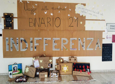 Foto con cartellone e materiale creato dagli studenti: nel cartellone è scritto "Viaggio della memoria Binario 21 Indiferrenza"